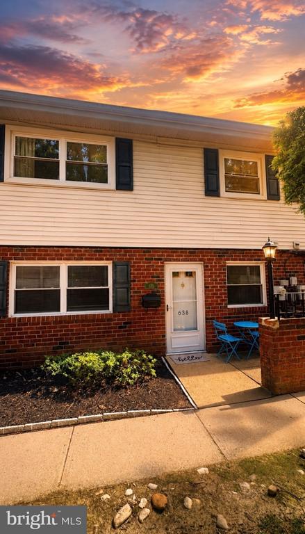 Two-story brick and siding home with blue patio chairs beneath a vivid sunset sky.