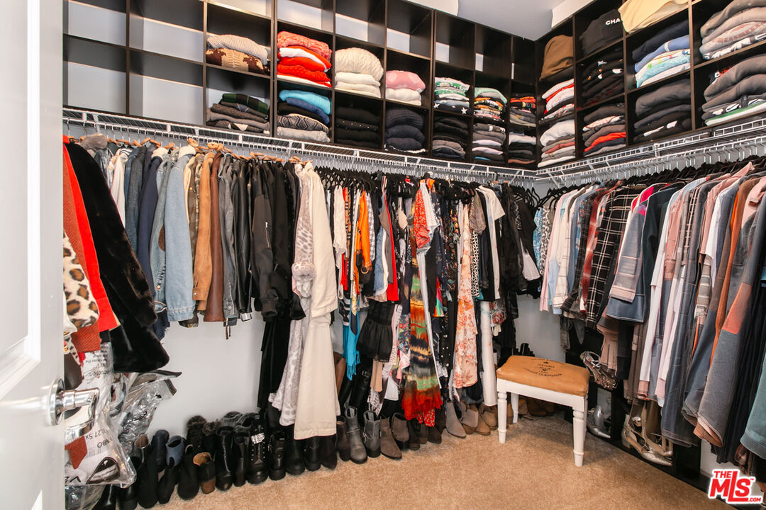 Walk-in closet with dark built-in shelving, clothing on three walls, floor-level shoes, and a small bench.