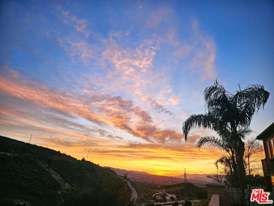 Sunset view over Santa Clarita hills and valley, framed by palm trees and part of a home.