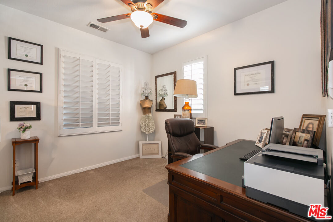 Home office with a wooden desk, printer, leather chair, and shuttered windows.
