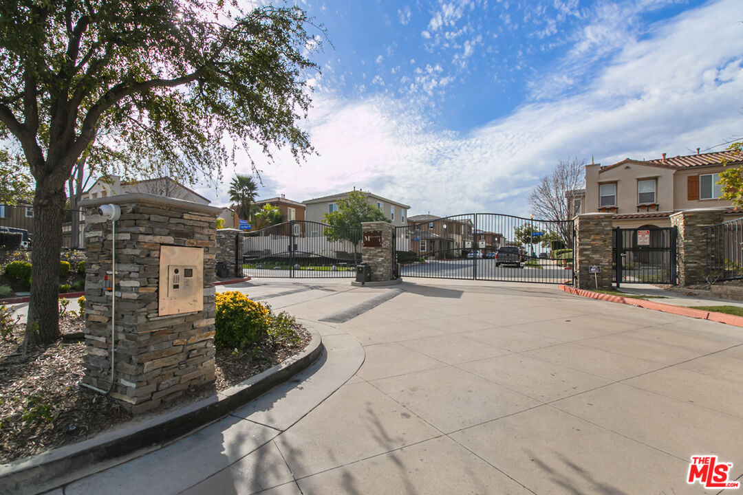 Gated community entrance with stone pillars and homes visible beyond the black metal gates.
