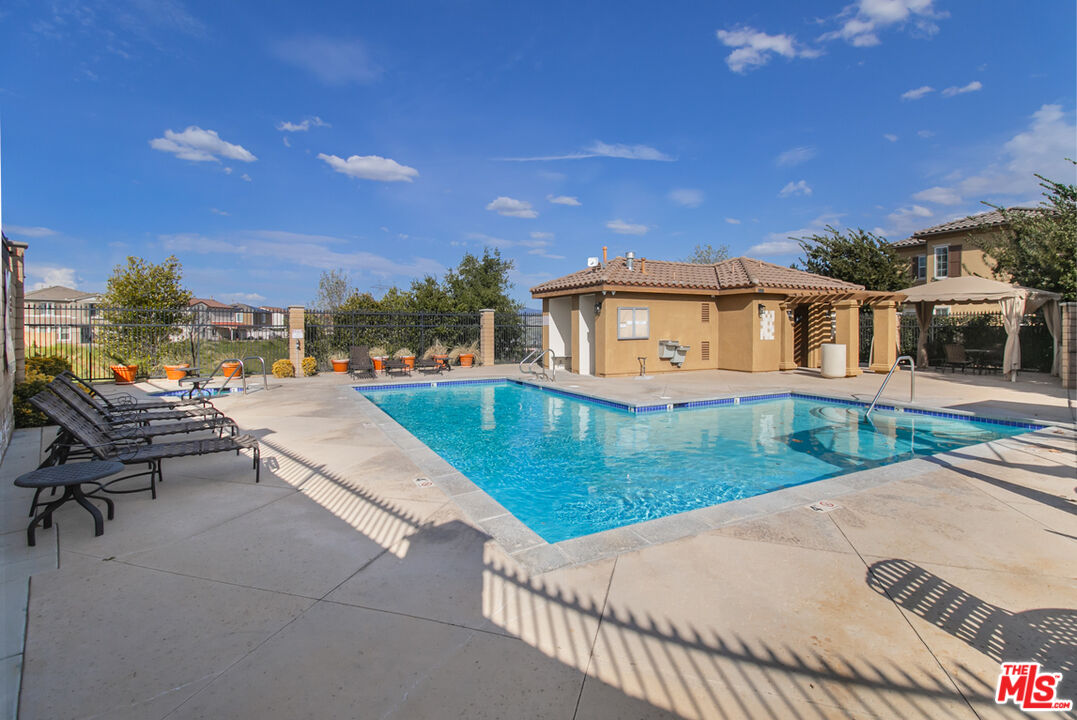 Backyard pool with lounge chairs and a covered seating area beside a tan house.