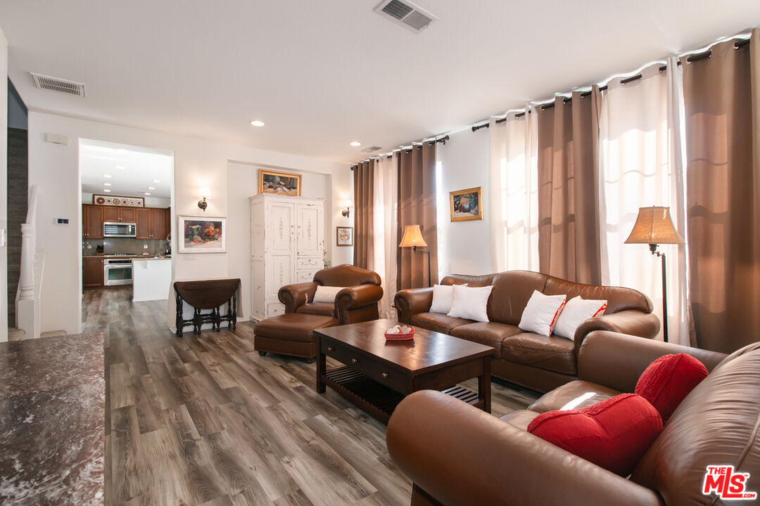 Living room with brown leather seating, wood-look floors, and tall curtained windows.