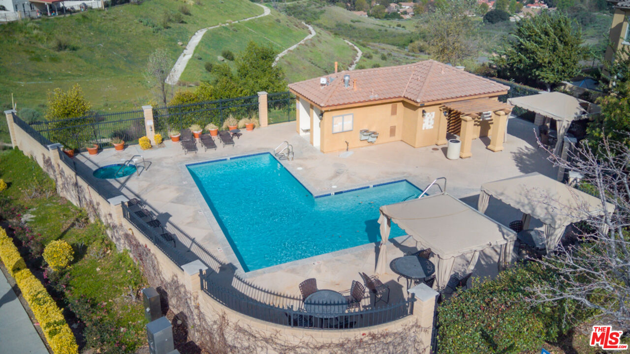 Aerial view of a backyard pool and spa beside a tan pool house and furnished patio.