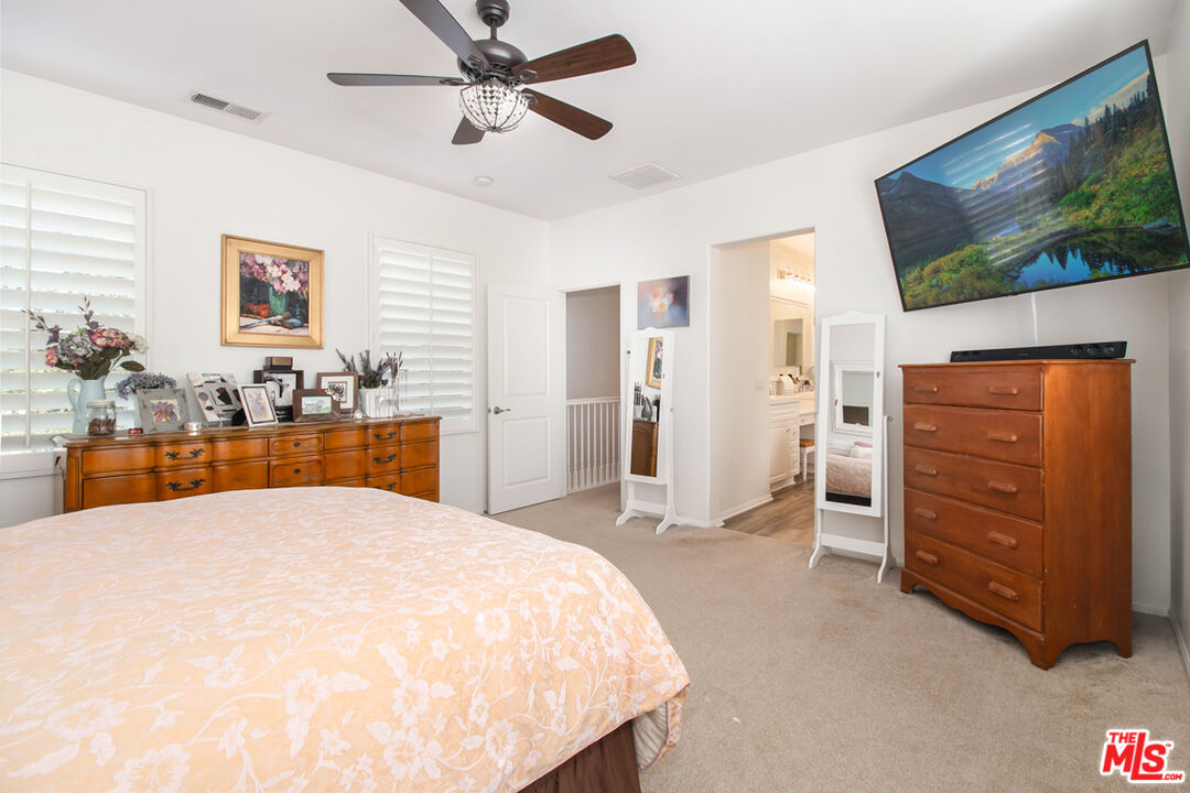 Bedroom with peach floral bedding, wooden dressers, plantation shutters, and a wall-mounted television.