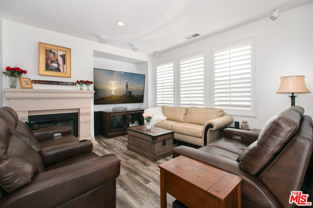 Living room with a fireplace, leather recliners, beige sofa, and plantation shutters.