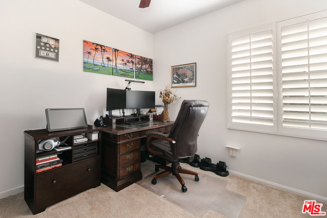 Home office with a dark wood desk, dual monitors, leather chair, and white plantation shutters.