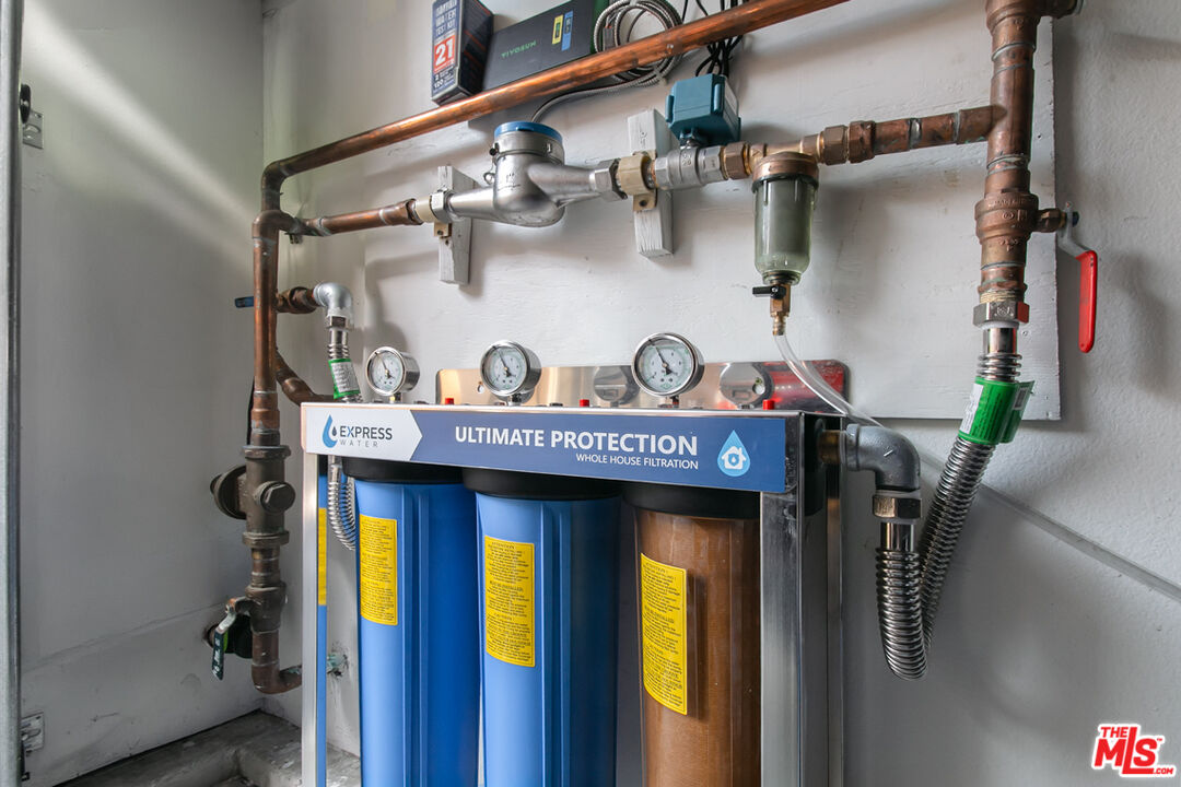 Whole-house water filtration system with three filter tanks, pressure gauges, and exposed copper pipes.