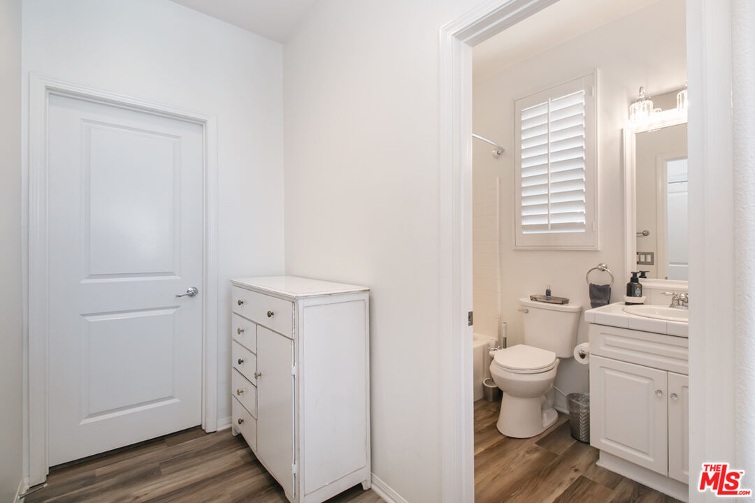 Bathroom with a white vanity and toilet, viewed through a doorway beside a small storage cabinet.