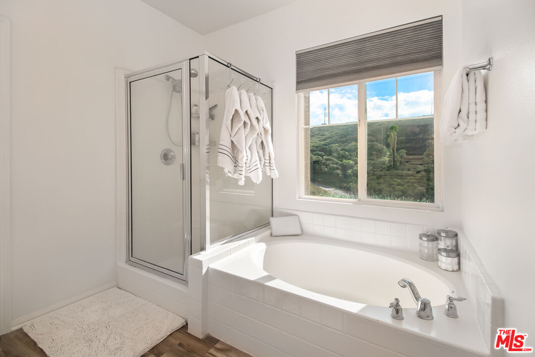 Bathroom with a large soaking tub, glass-enclosed shower, and window overlooking green hills.