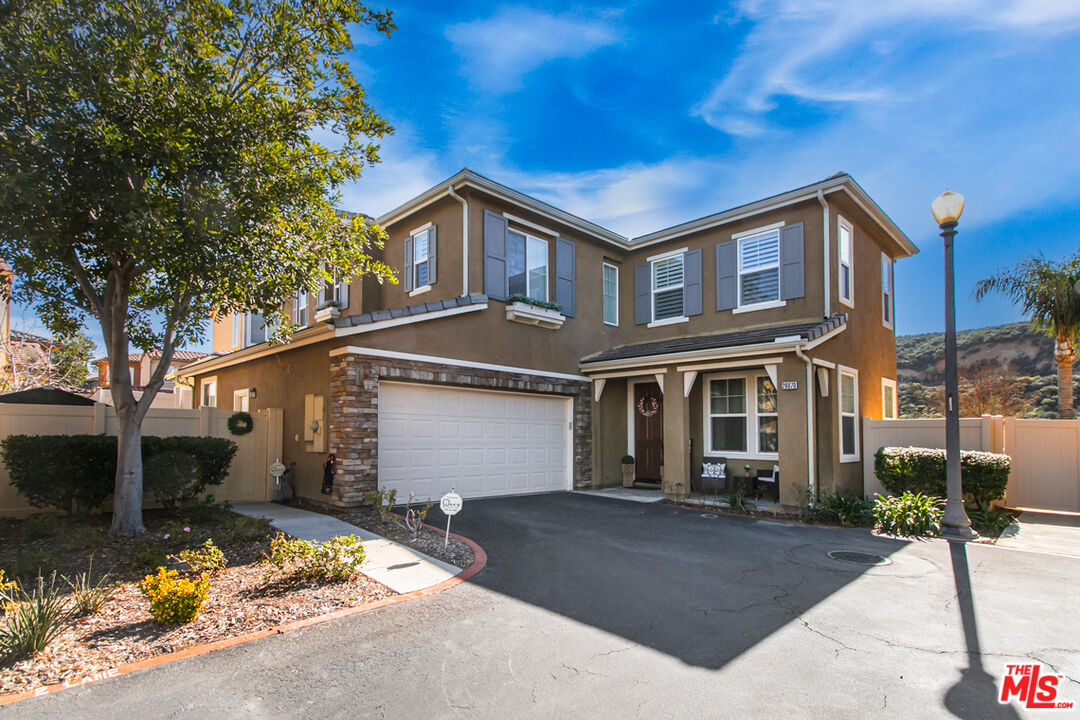 Two-story brown stucco home with stone accents, an attached garage, and a wide driveway.