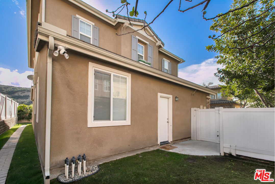 Two-story tan stucco house with a fenced patio and narrow side lawn.