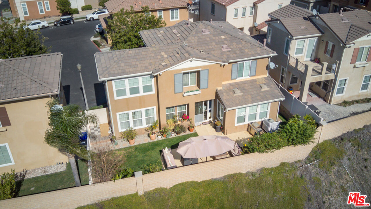Aerial view of a tan two-story home with a fenced backyard and umbrella-covered patio.