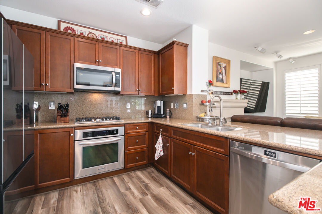Kitchen with wood cabinetry, granite counters, stainless steel appliances, and wood-look flooring.