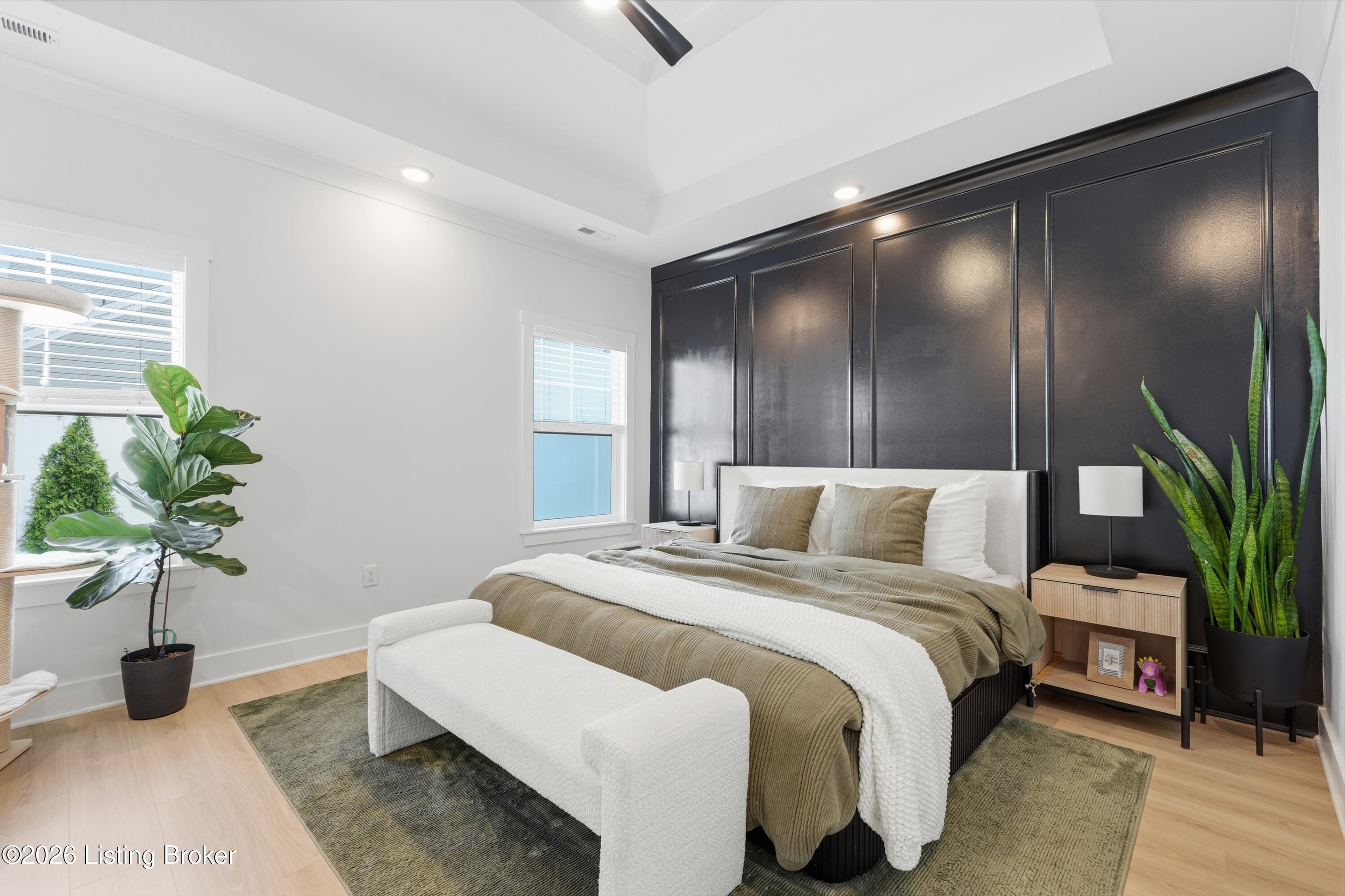 Staged bedroom with a paneled charcoal accent wall, king bed, and bench beneath a vaulted ceiling.