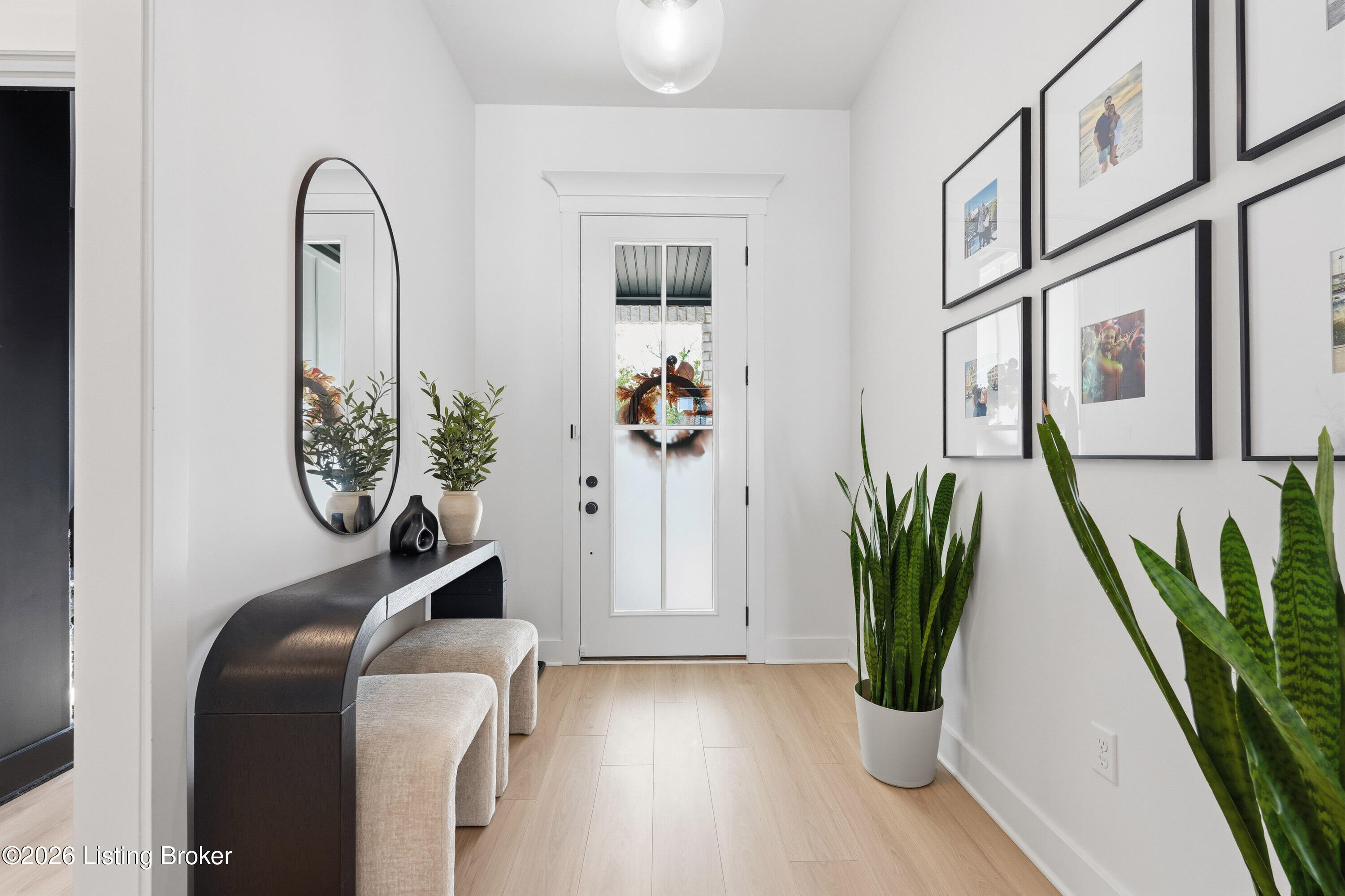 Bright entry foyer with a glass-paneled front door, console table, oval mirror, and framed photos.