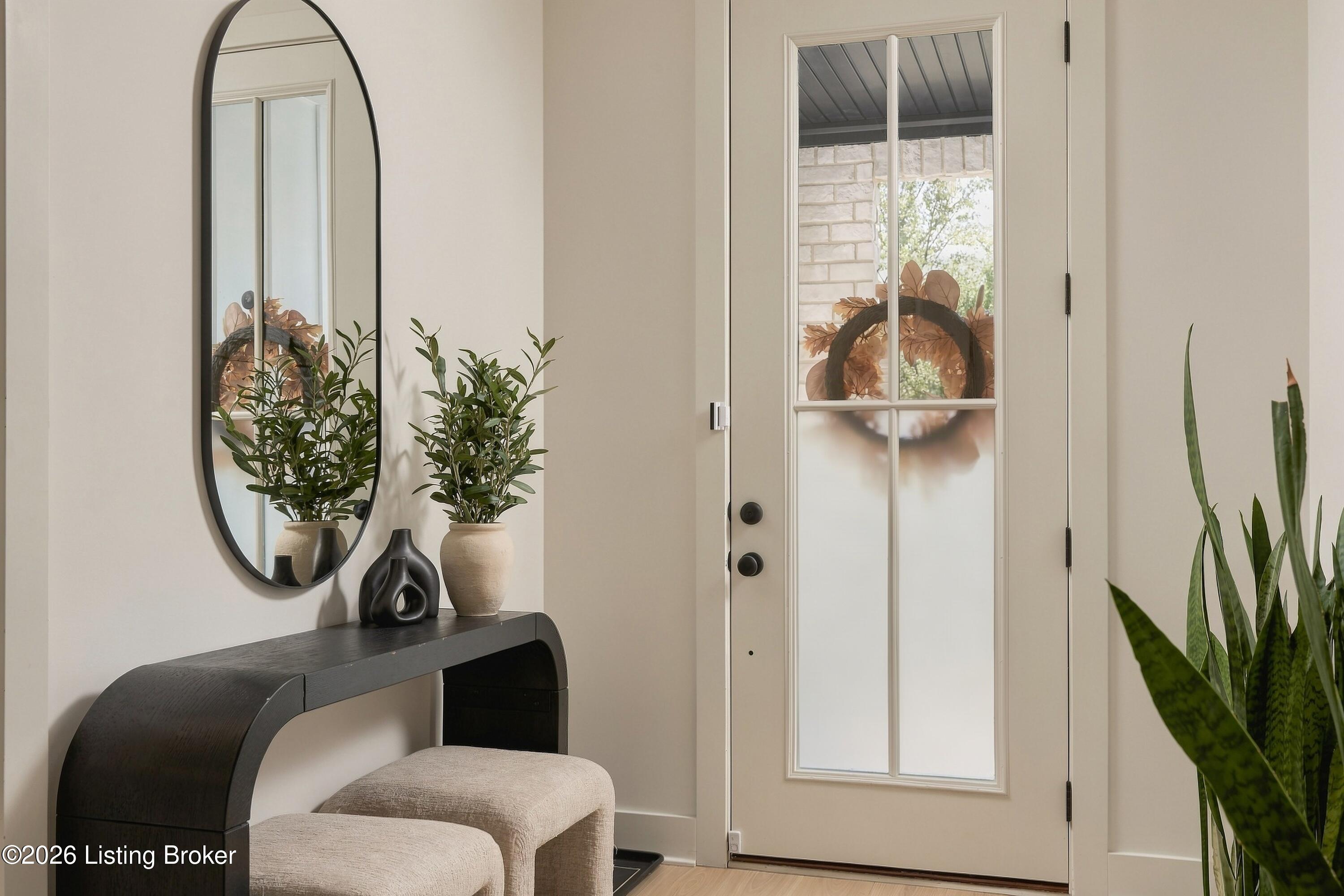 Entryway with a glass-paneled front door, dark console table, oval mirror, and upholstered bench.
