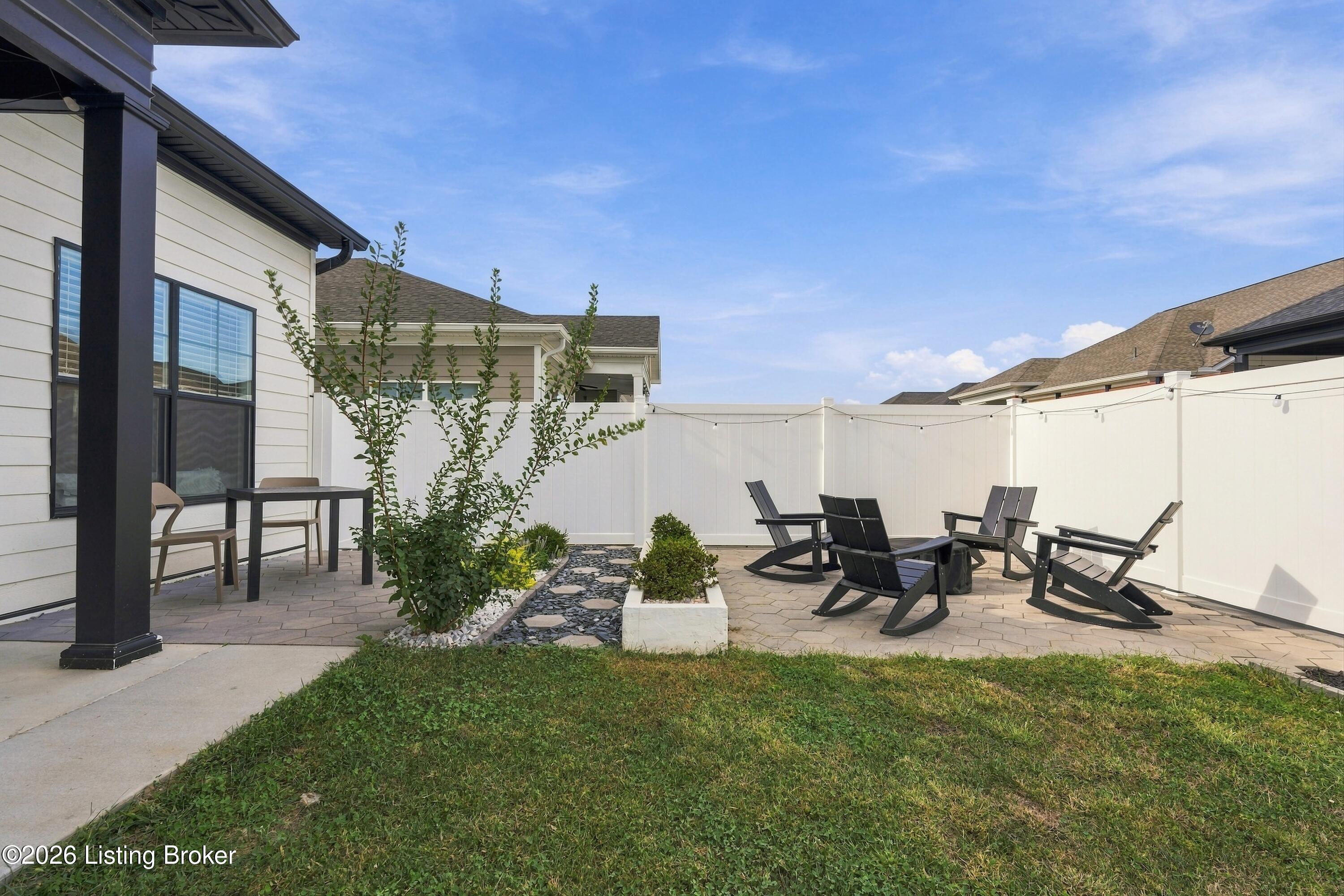 Fenced backyard patio with black lounge chairs, pavers, and a landscaped garden bed.