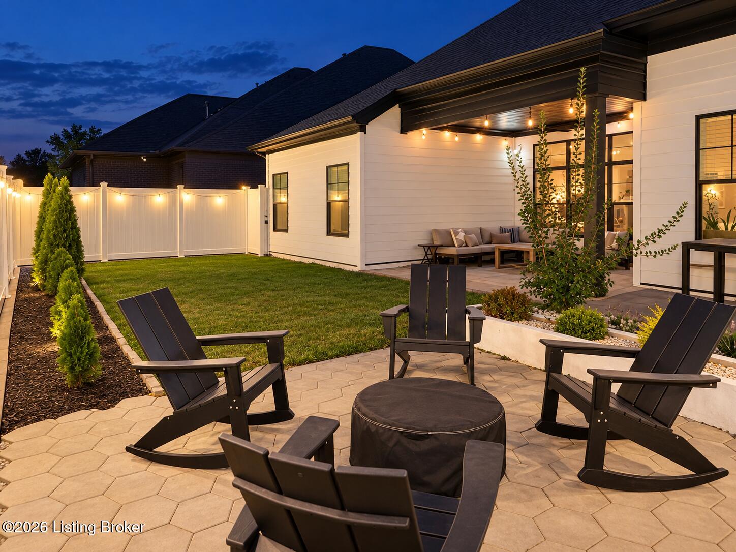 Backyard patio with Adirondack chairs, a fire pit, and a covered outdoor seating area at dusk.