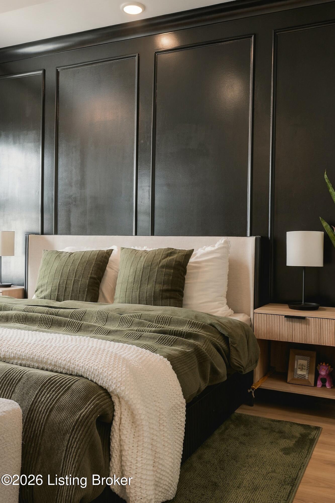 Bedroom with an upholstered bed, olive-green bedding, and a dark paneled accent wall.