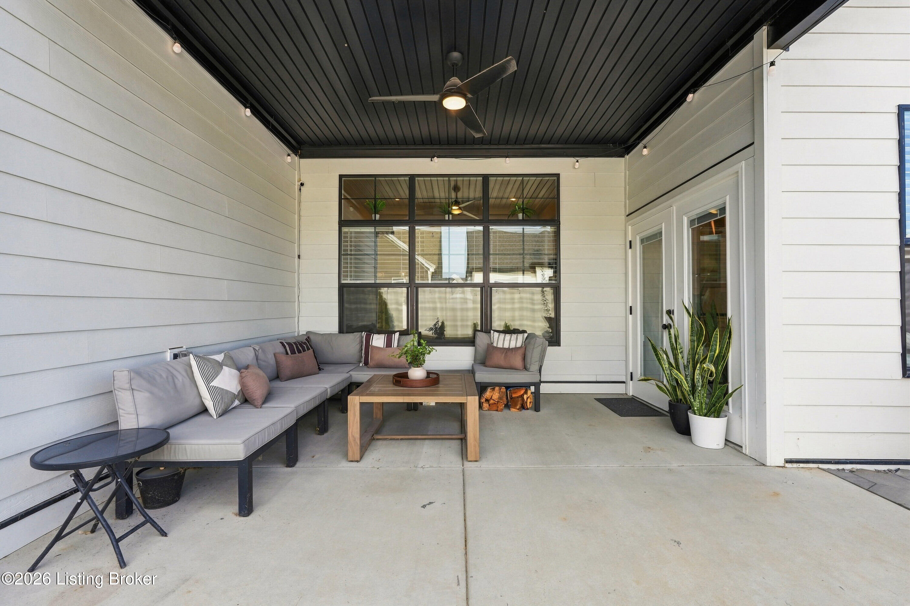 Covered patio with a gray sectional, wood coffee table, ceiling fan, and string lights.