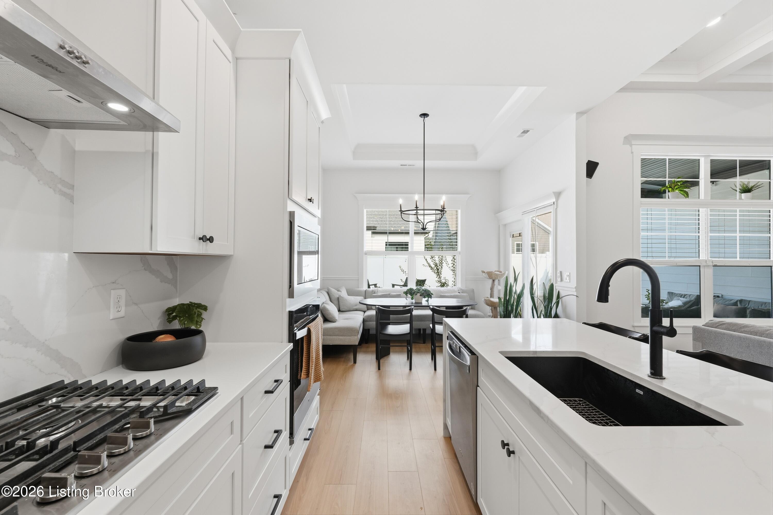 Bright white kitchen with a large island, black sink, and dining area beyond.