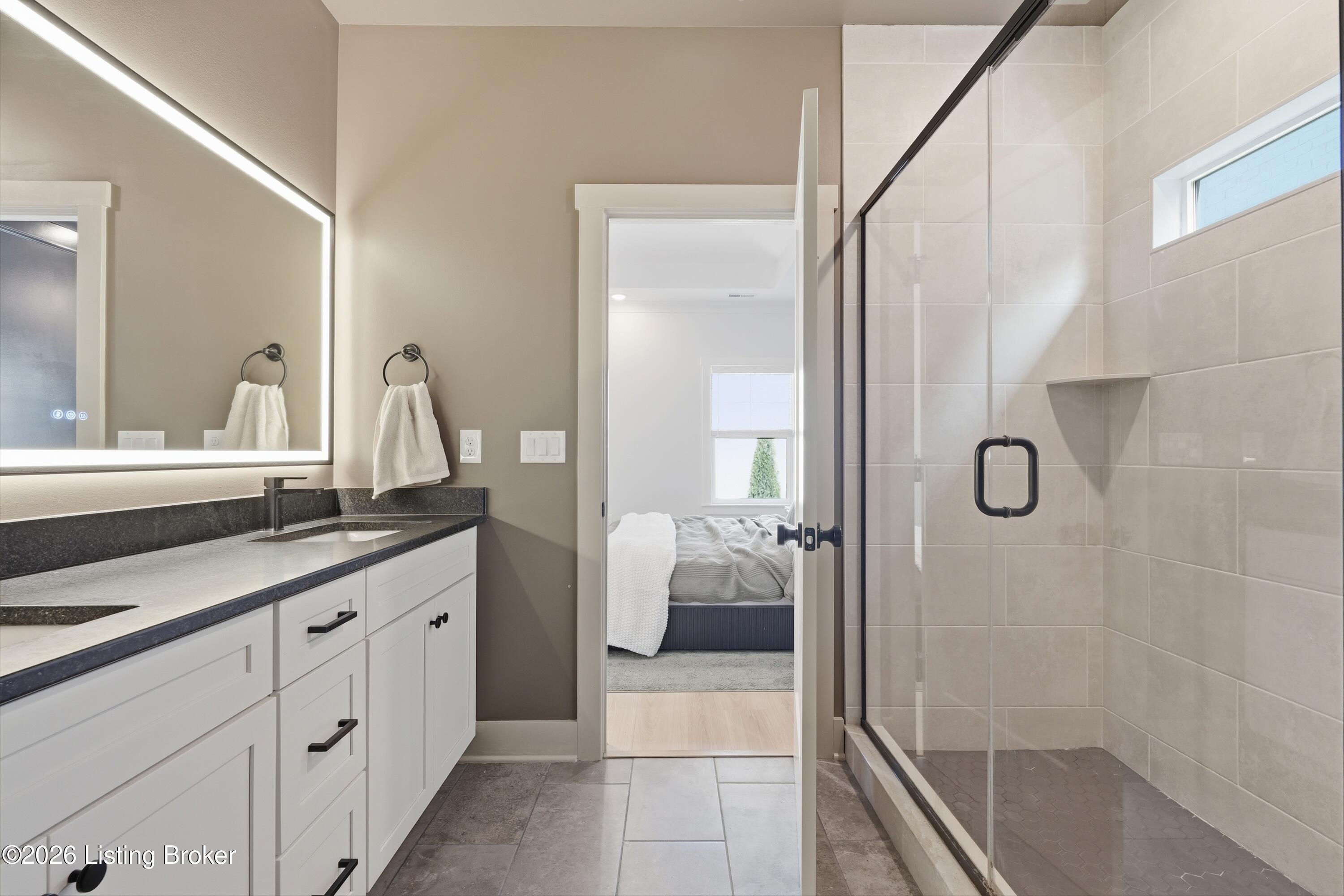 Bathroom with a double vanity, illuminated mirror, and glass-enclosed tiled shower.