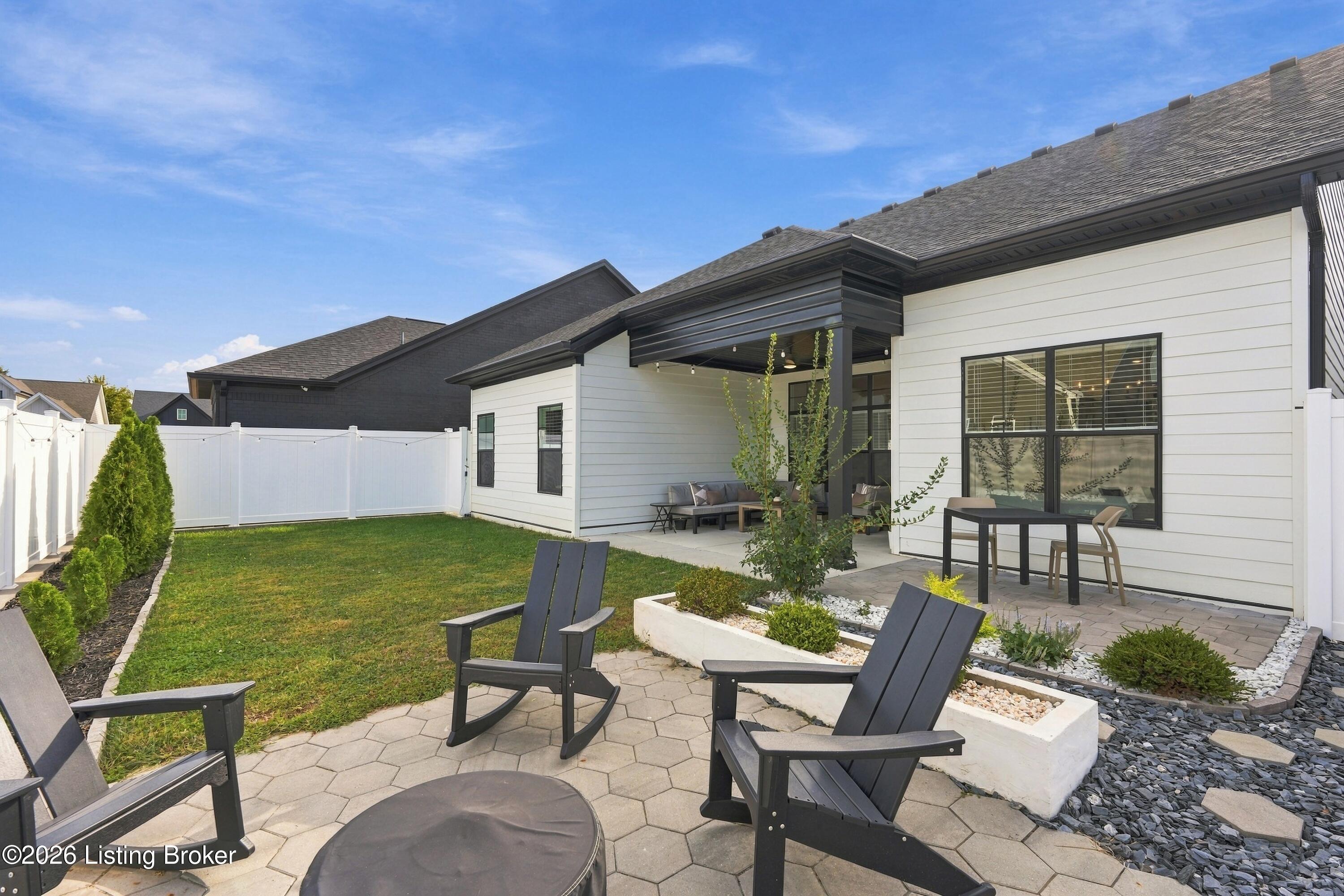 Modern white home with a fenced backyard, stone patio, and covered outdoor seating.