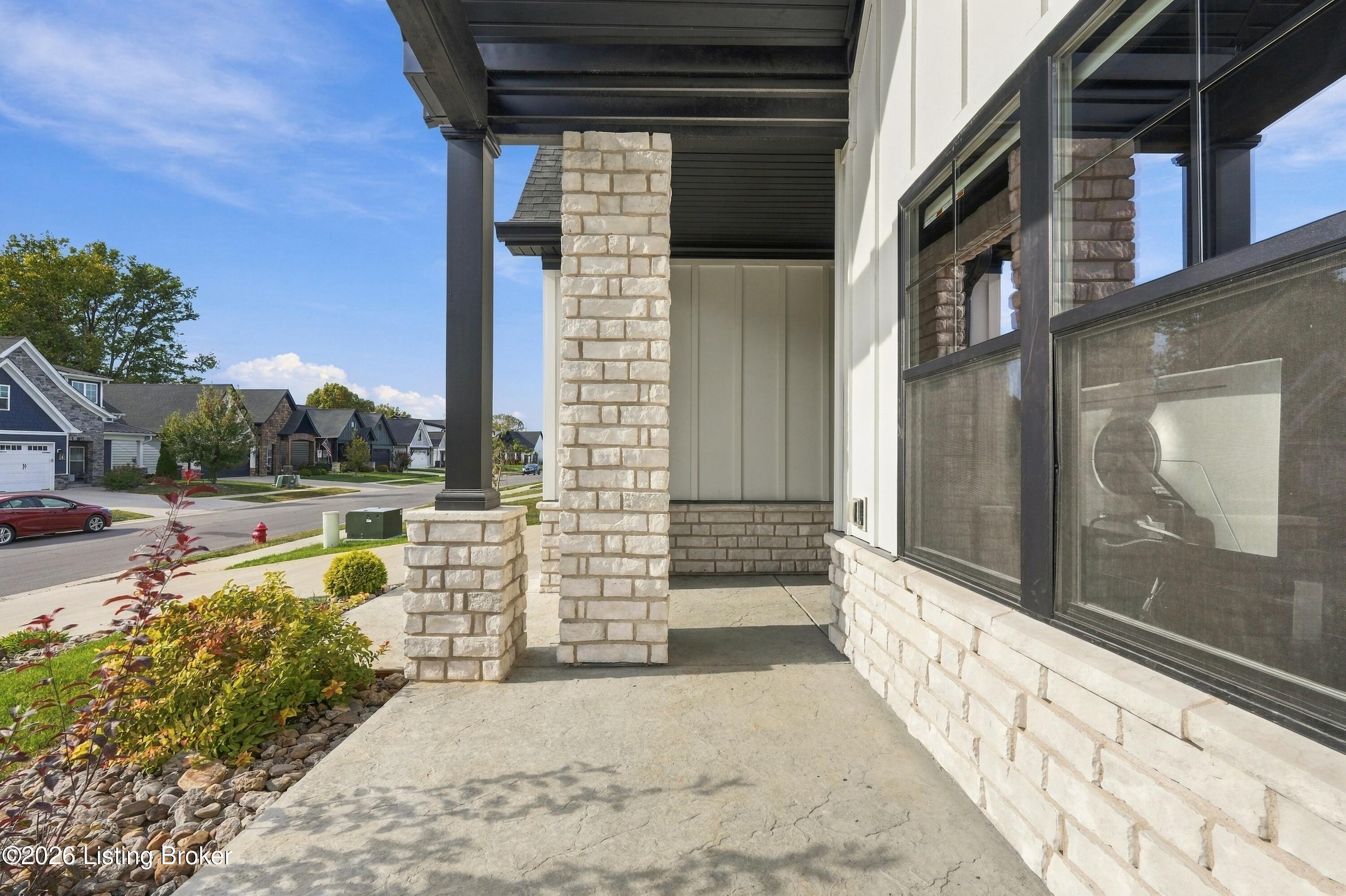 Covered front porch with pale stone pillars, dark trim, and landscaped entry walkway.