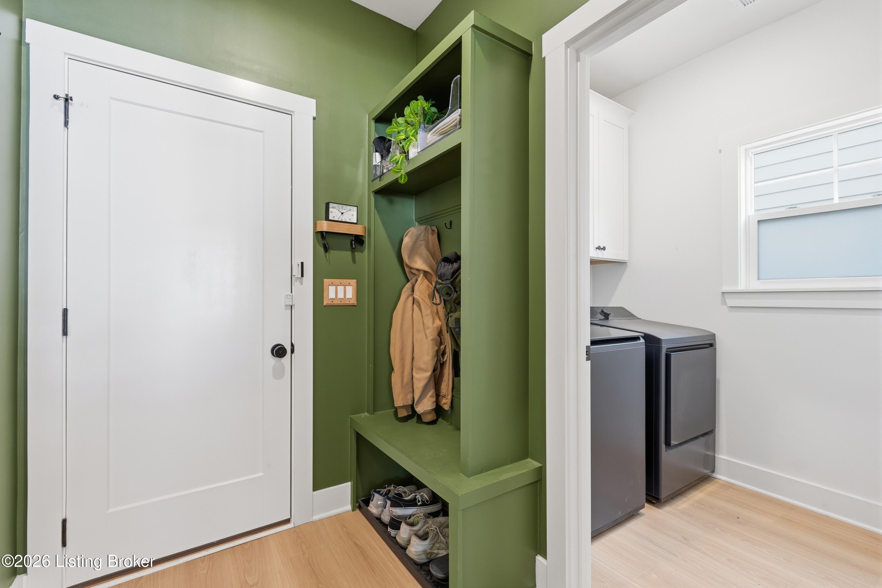 Mudroom with green built-in storage, a bench, coat hooks, and an adjoining laundry room.