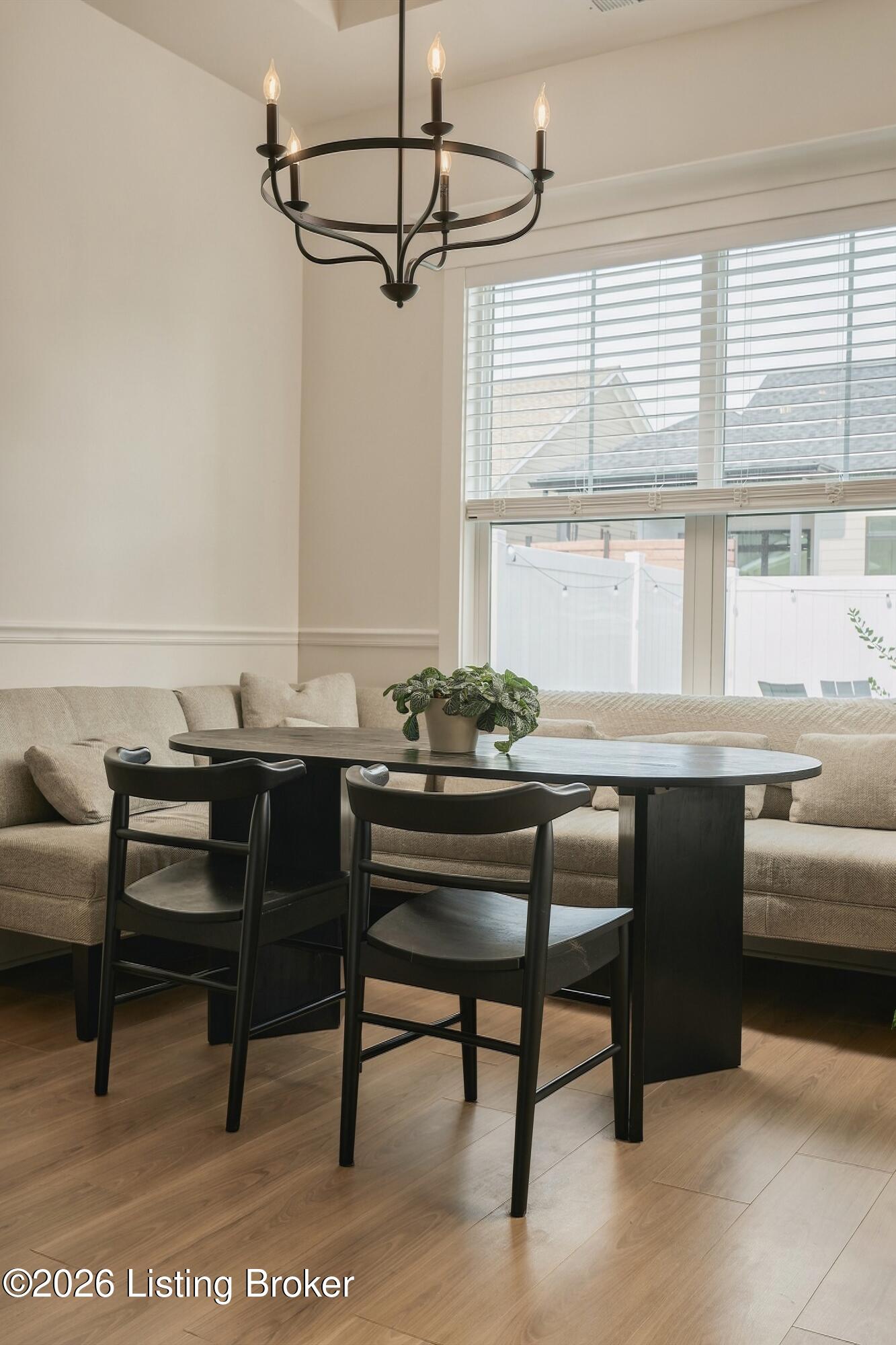 Dining area with a curved banquette, dark table and chairs, and a black ring chandelier.