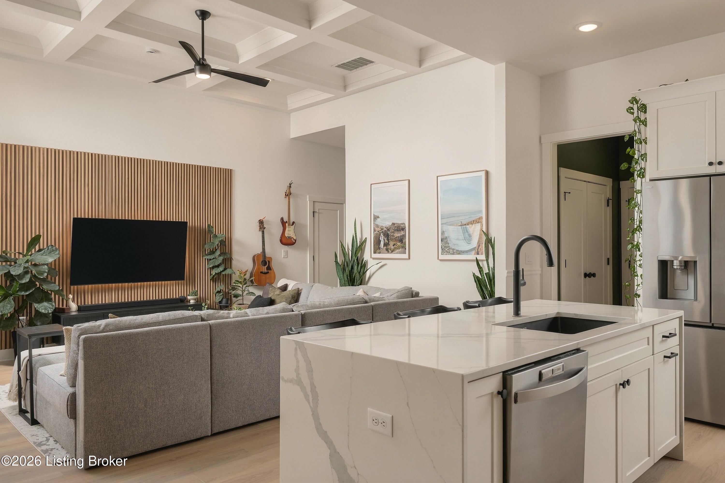 Open-plan kitchen and living room with a marble island, coffered ceiling, and wood-slat TV wall.