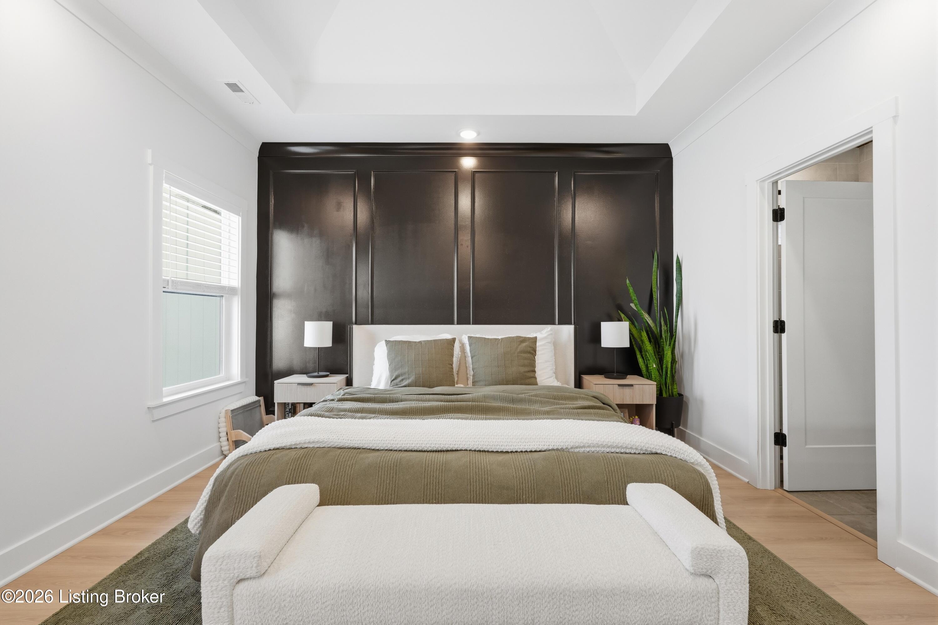 Staged bedroom with an olive-green bedspread, dark paneled accent wall, and tall snake plant.