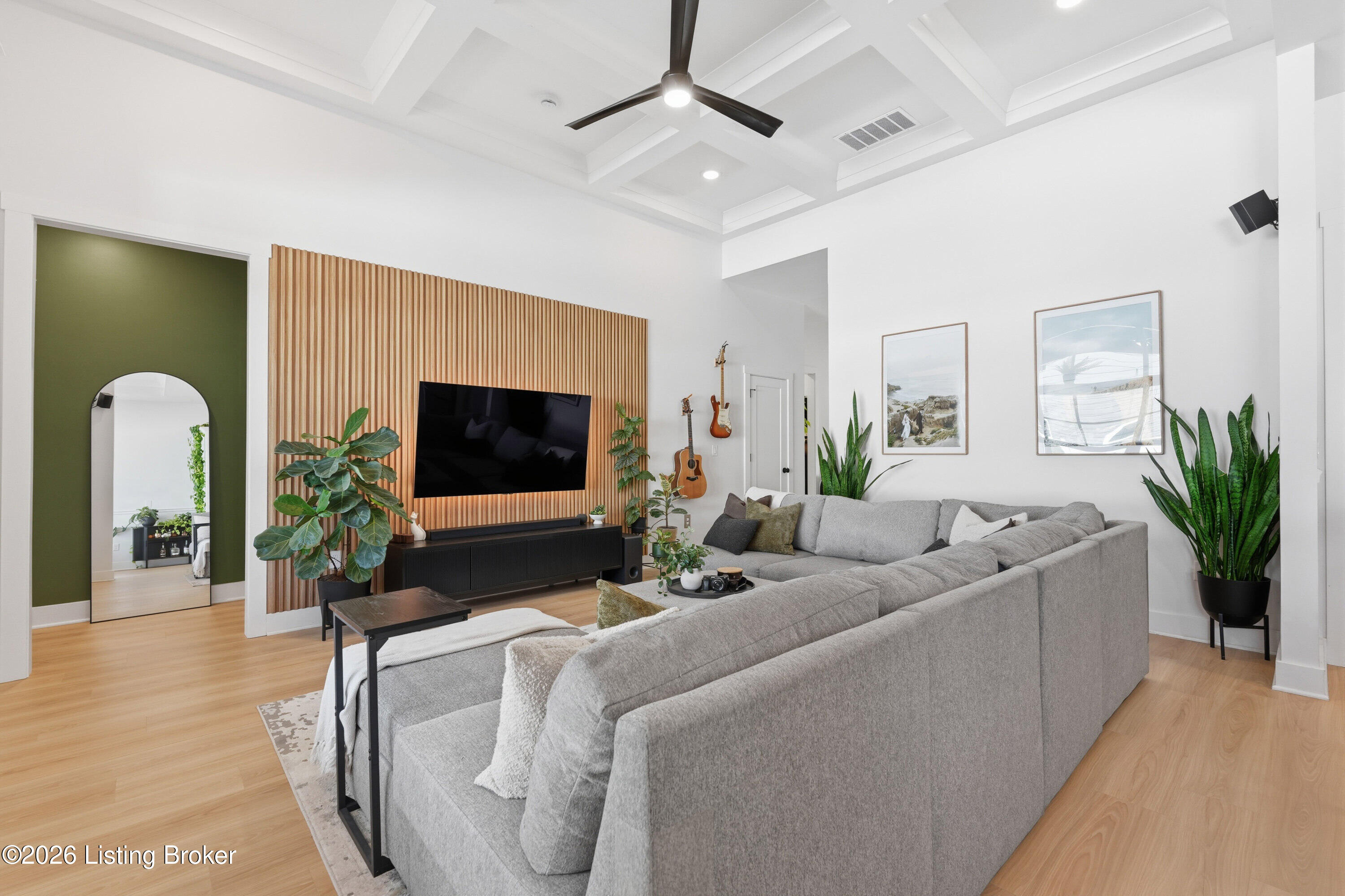 Living room with a gray sectional, wood-slat TV wall, and sculpted ceiling.