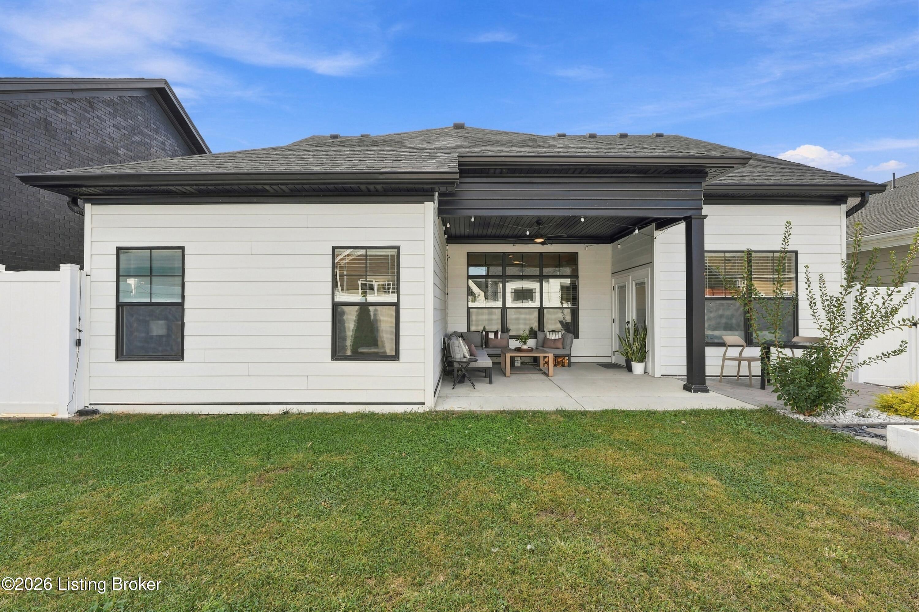 Rear of a white-sided home with a furnished, covered patio and lawn.