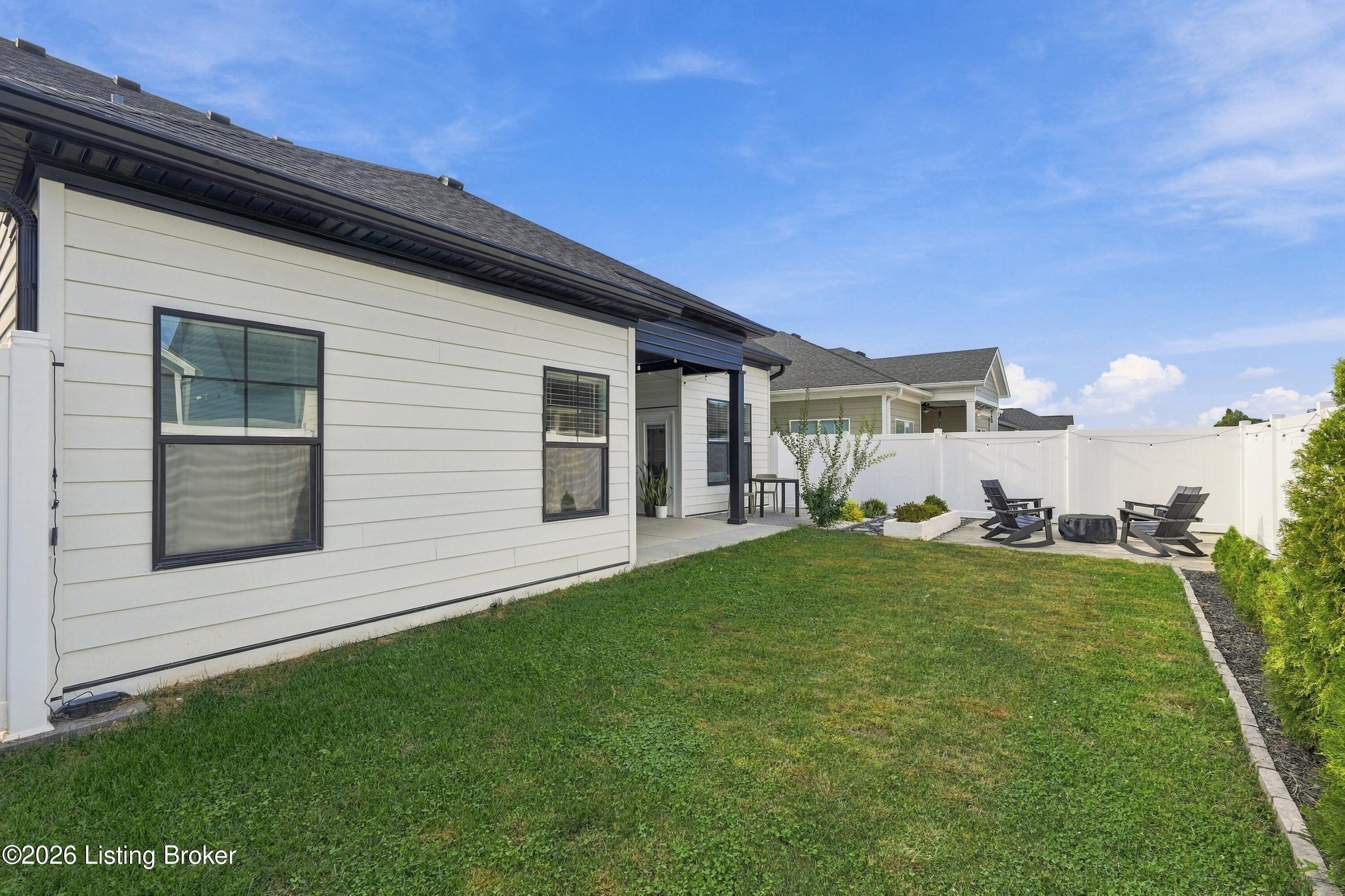 Rear yard with a covered patio, lawn, white privacy fence, and outdoor seating.