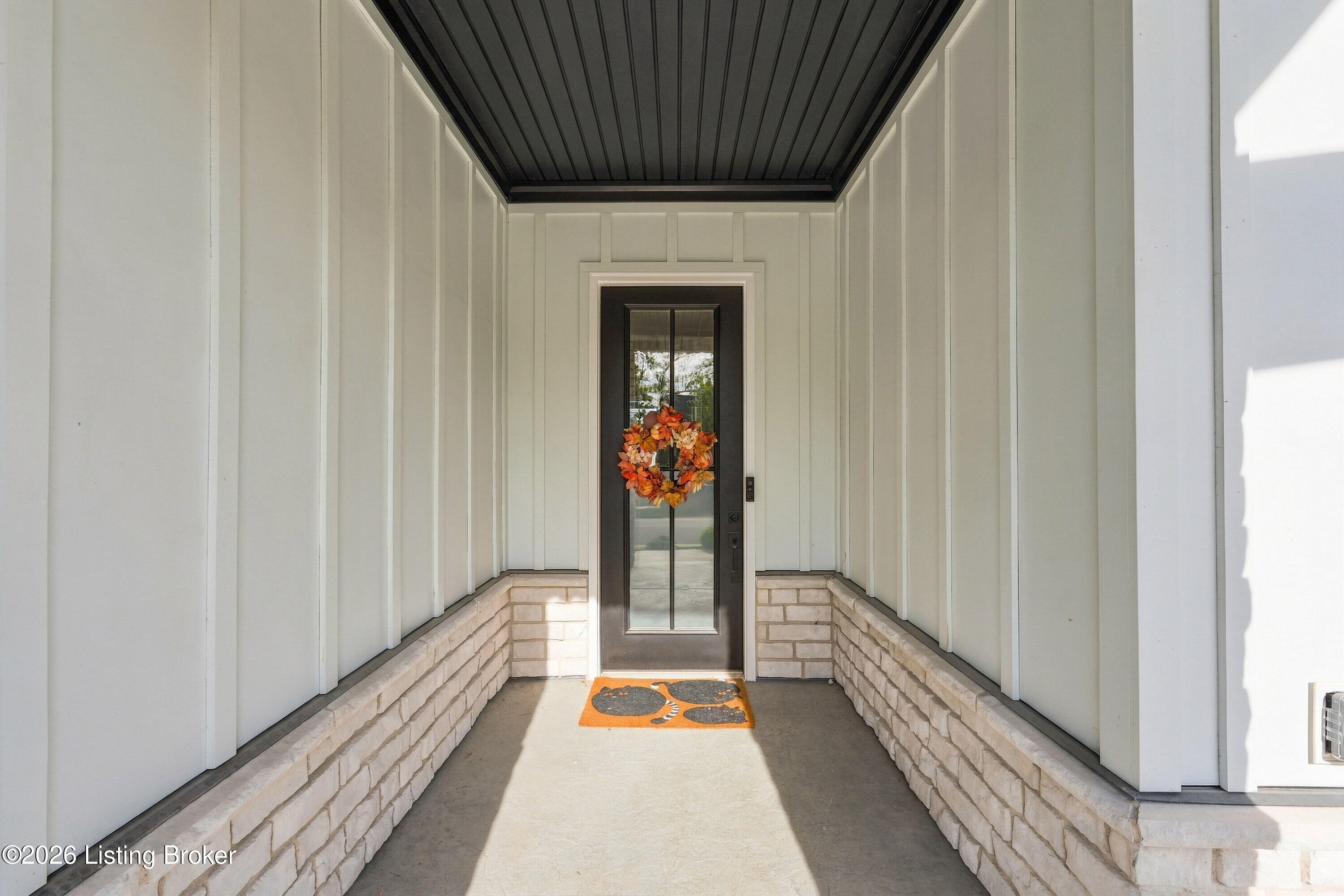 Covered front entry with a dark glass door, autumn wreath, and stone porch walls.