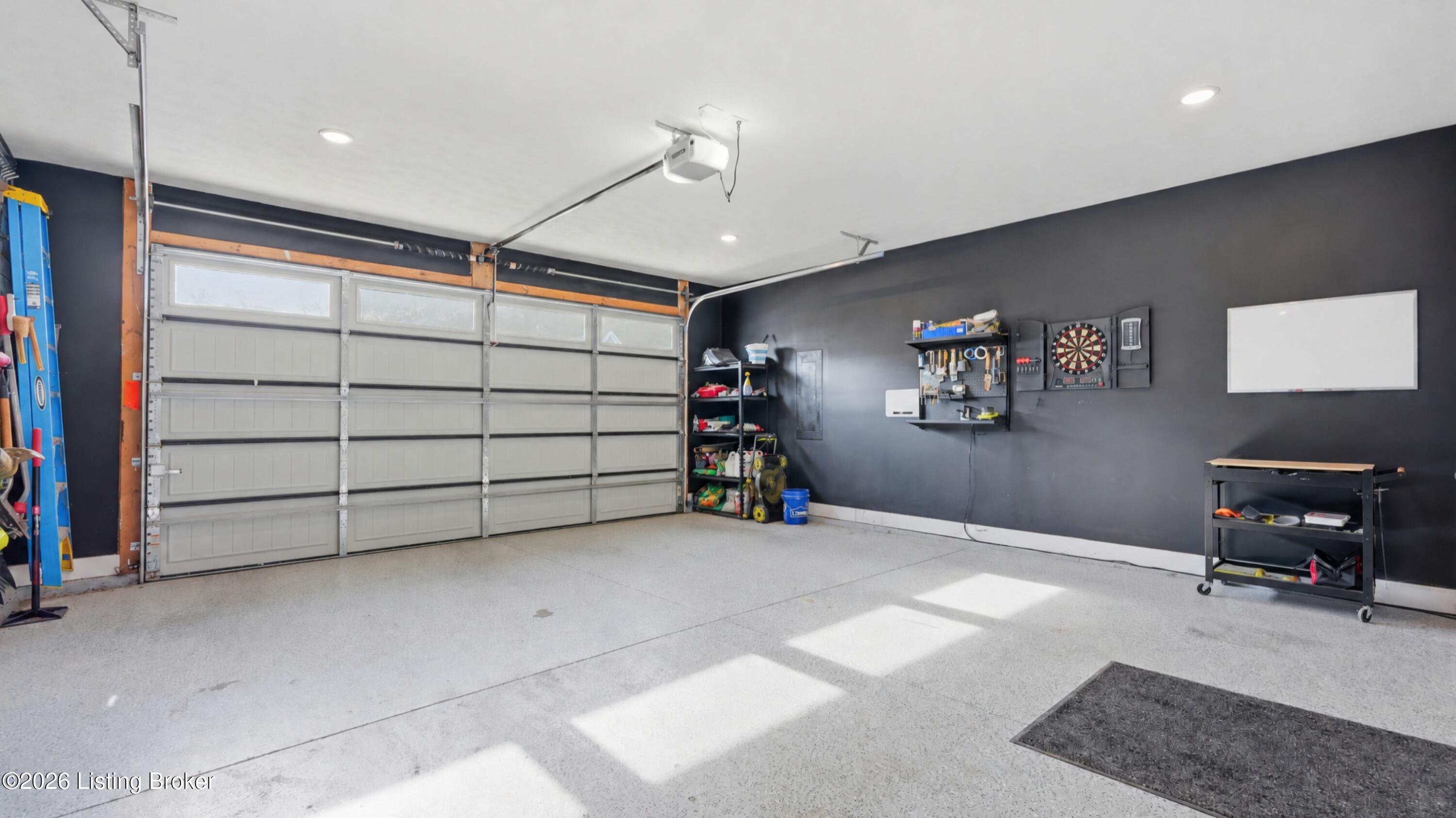 Garage with a wide sectional door, dartboard, wall-mounted tool storage, and bright speckled floor.