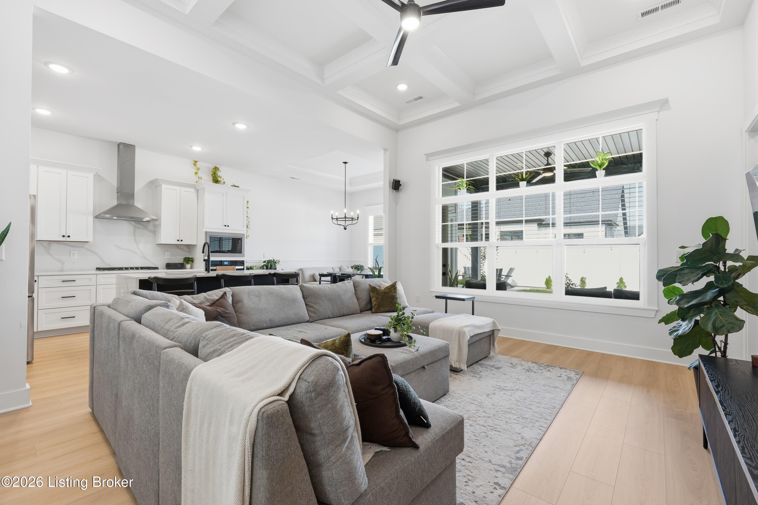 Open-plan living room and kitchen with a gray sectional, white cabinetry, and large windows.