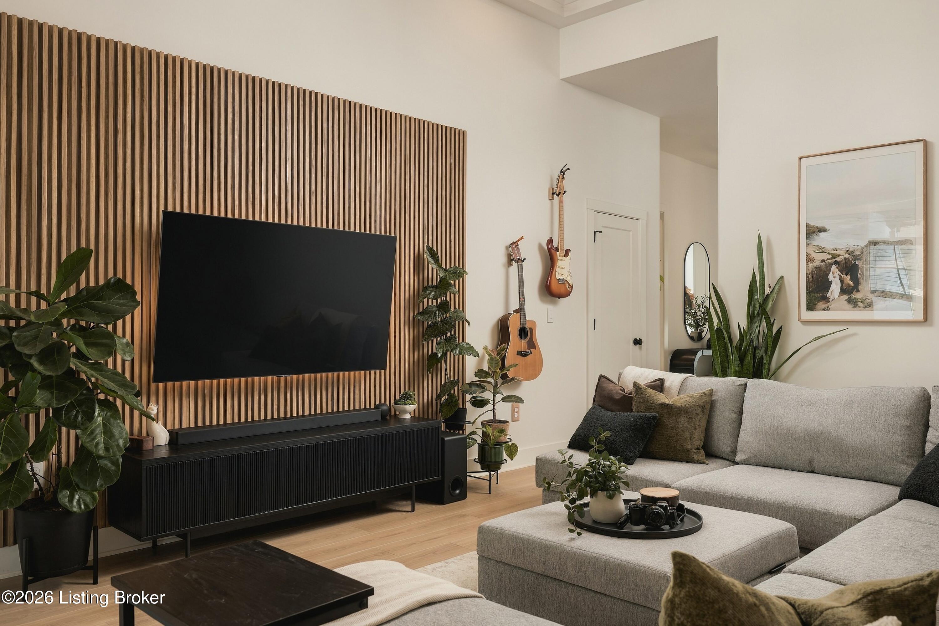 Living room with a gray sectional, wood-slat TV wall, and guitars displayed on the wall.