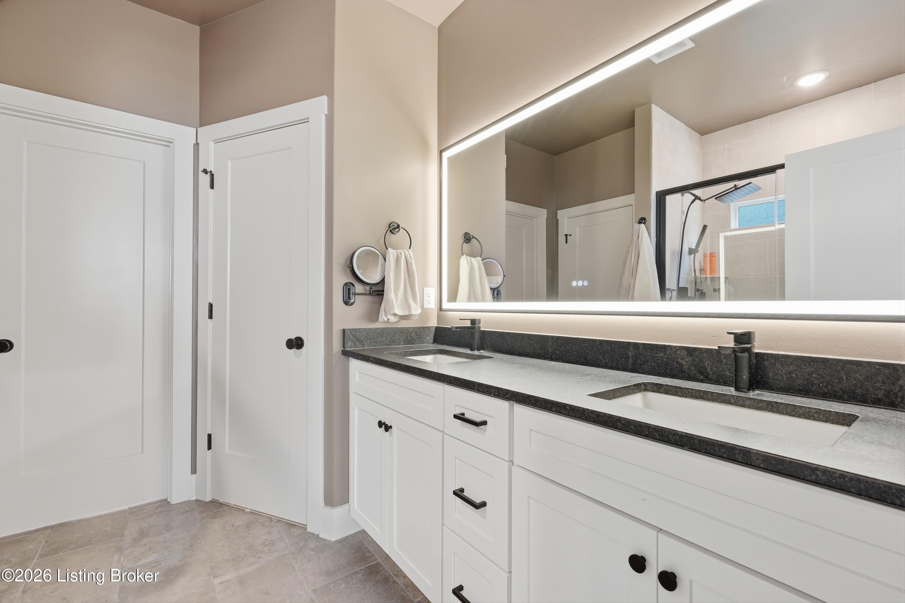 Bathroom with a double vanity, illuminated mirror, and glass-enclosed shower.