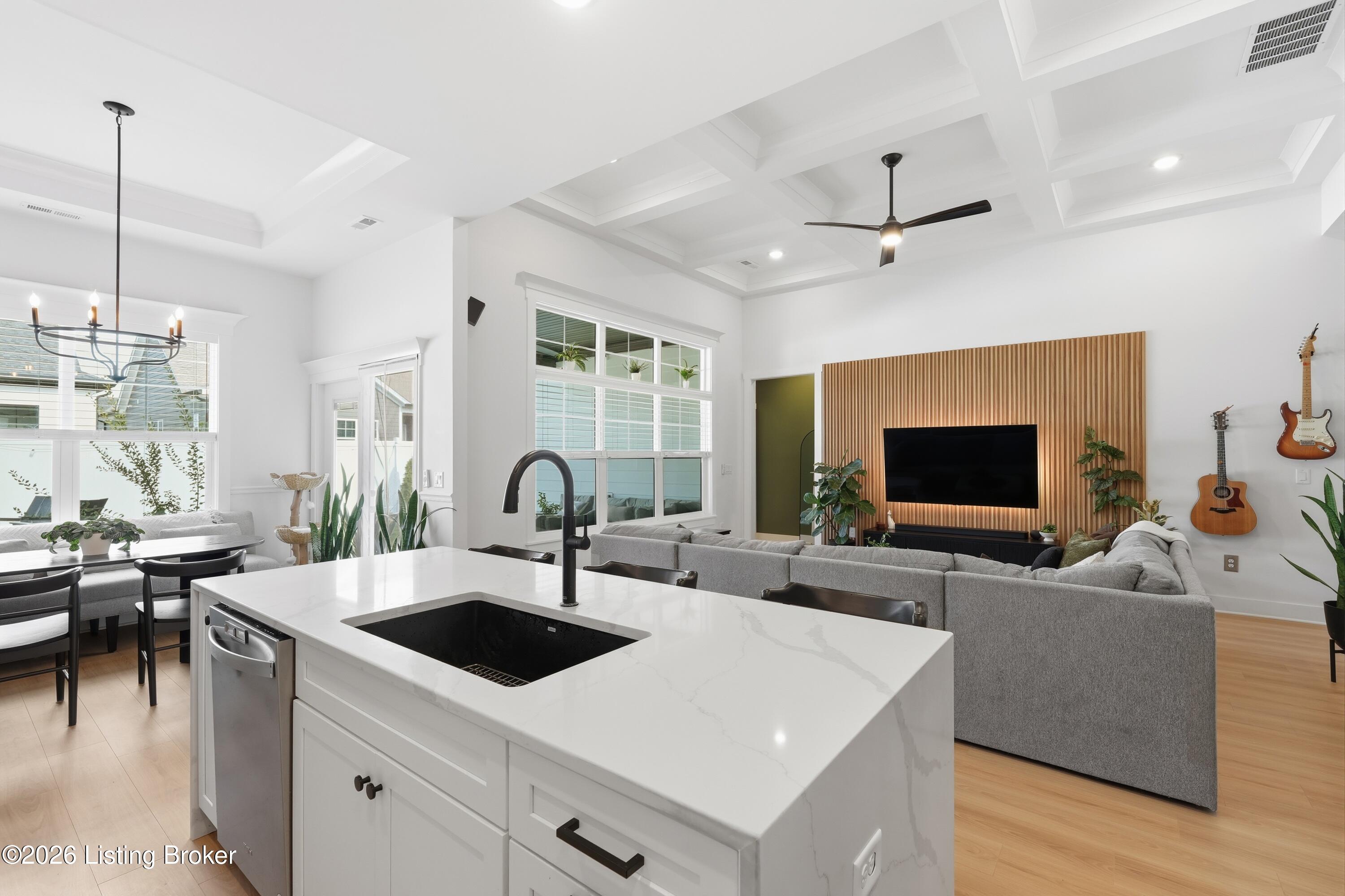 Open-plan kitchen and living room with a large marble island, tray ceiling, and wood-slat TV wall.