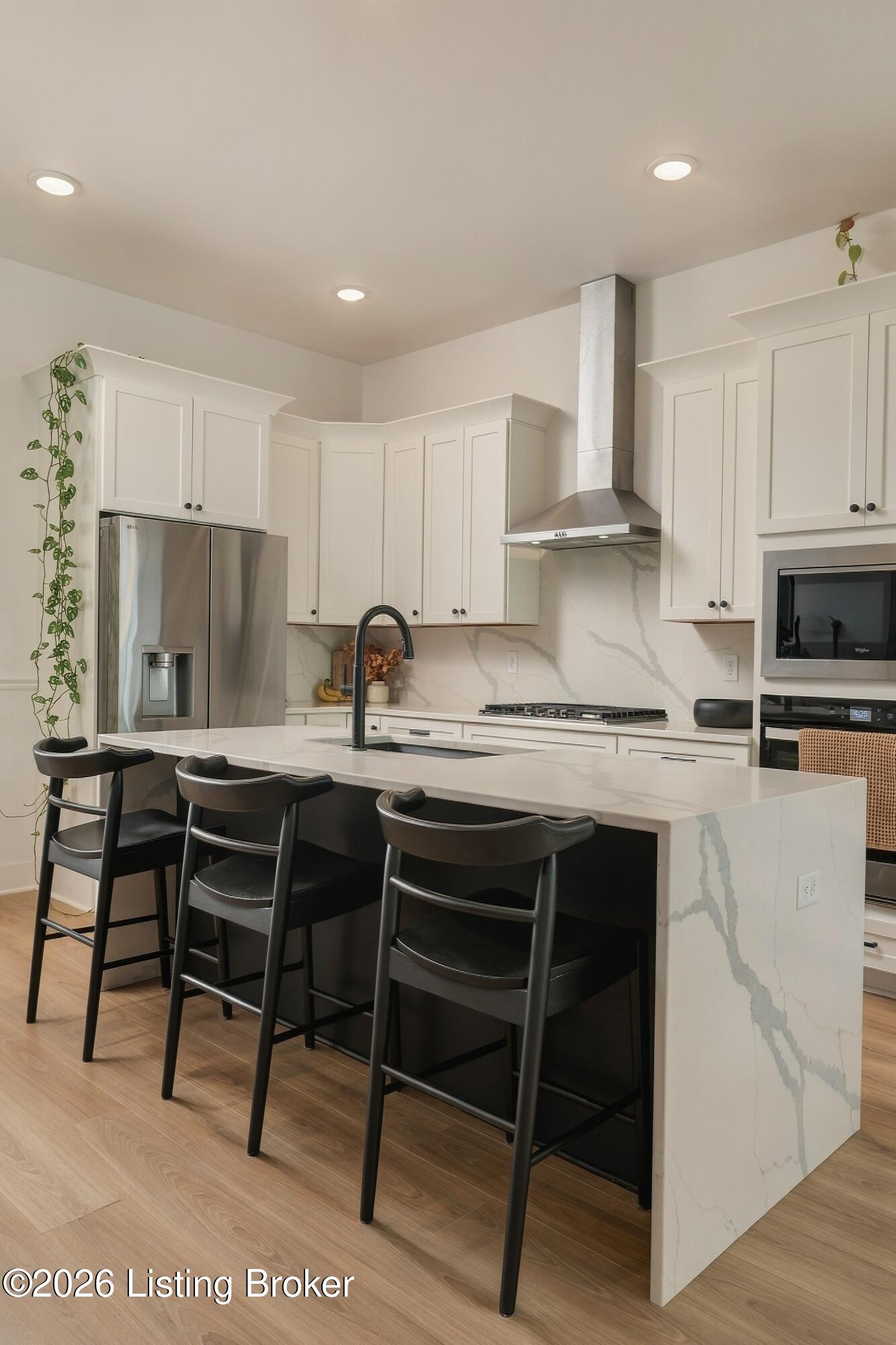 Bright kitchen with white cabinets, marble-veined island, stainless appliances, and three black barstools.
