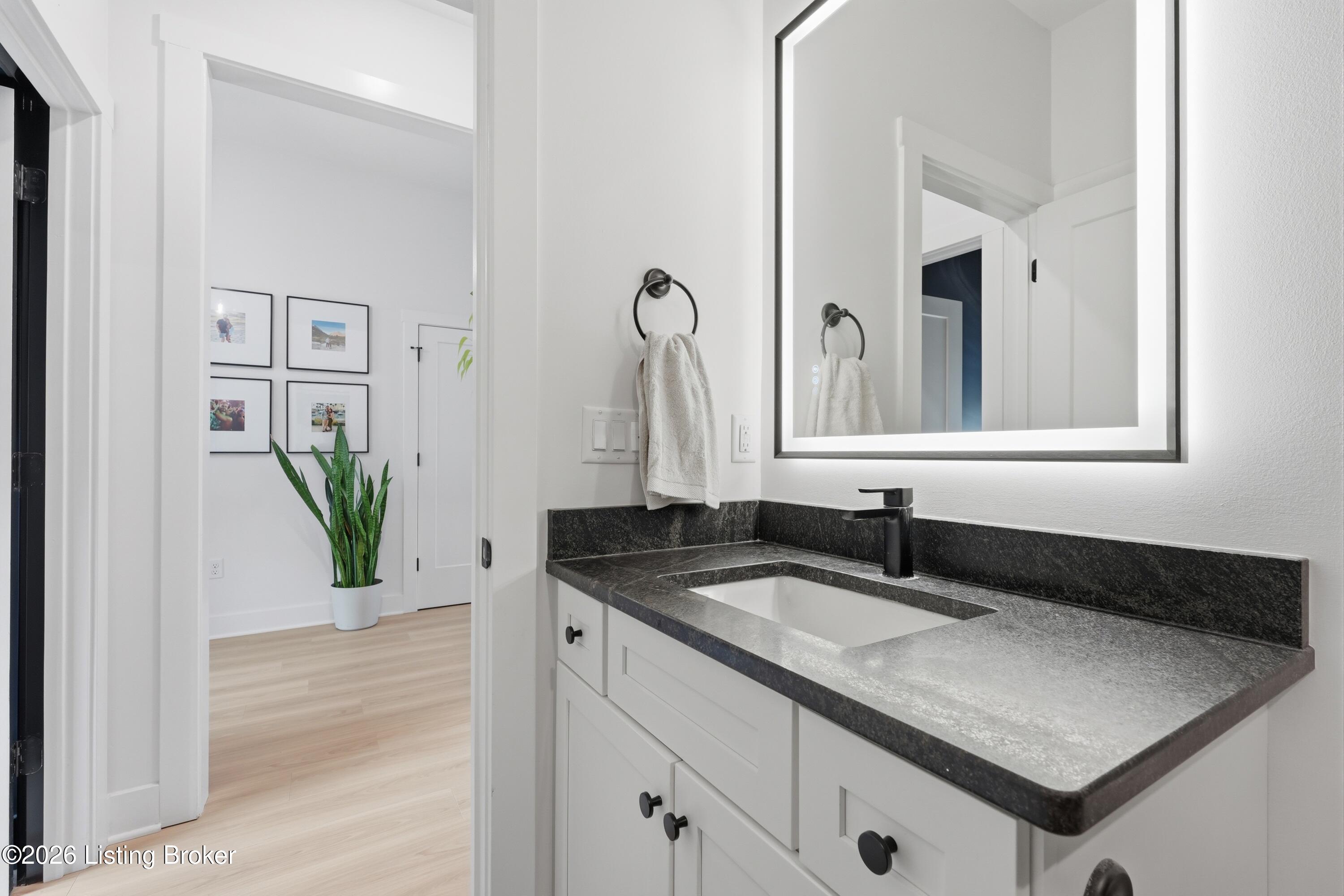 Bathroom vanity with dark stone countertop, rectangular sink, black faucet, and illuminated mirror.