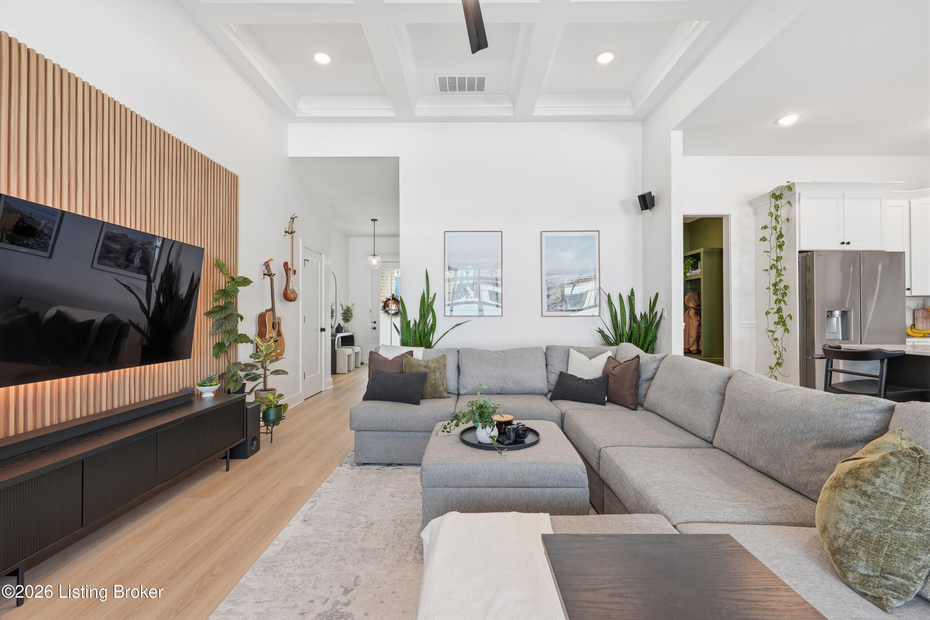 Living room with a gray sectional, wood-slat TV wall, and open kitchen.