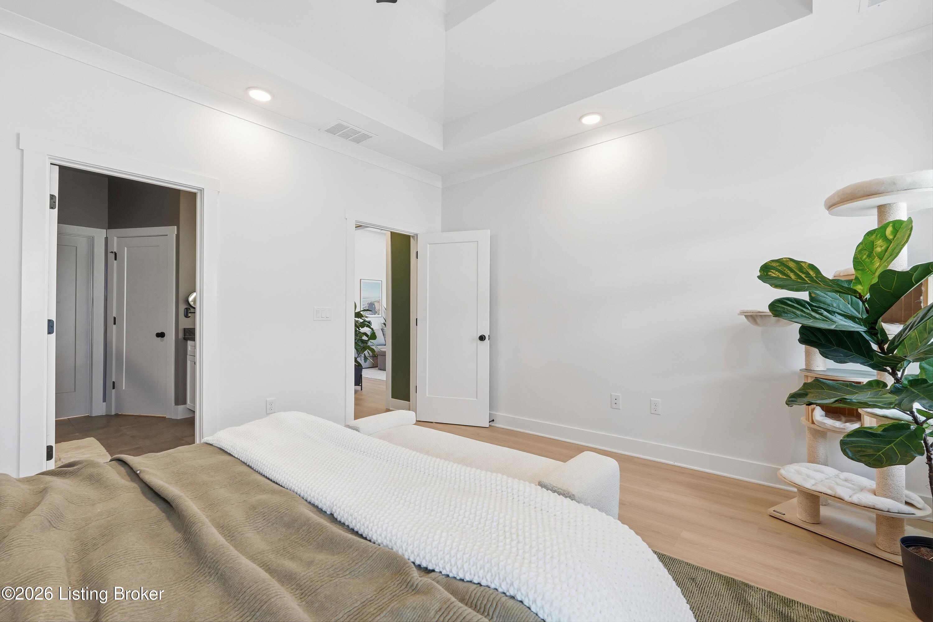 Bright bedroom with a layered bed, vaulted ceiling, and large cat tree beside a fiddle-leaf fig.