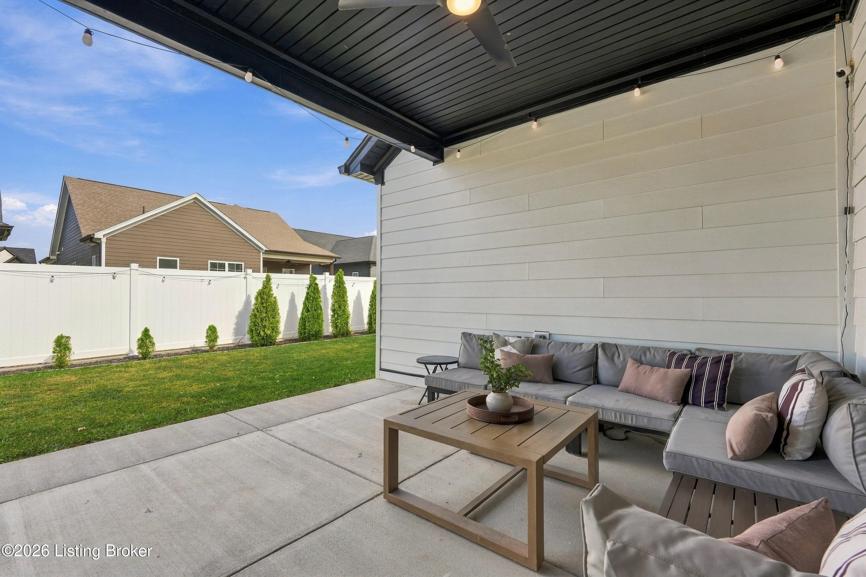 Covered patio with sectional seating, string lights, and a fenced lawn.