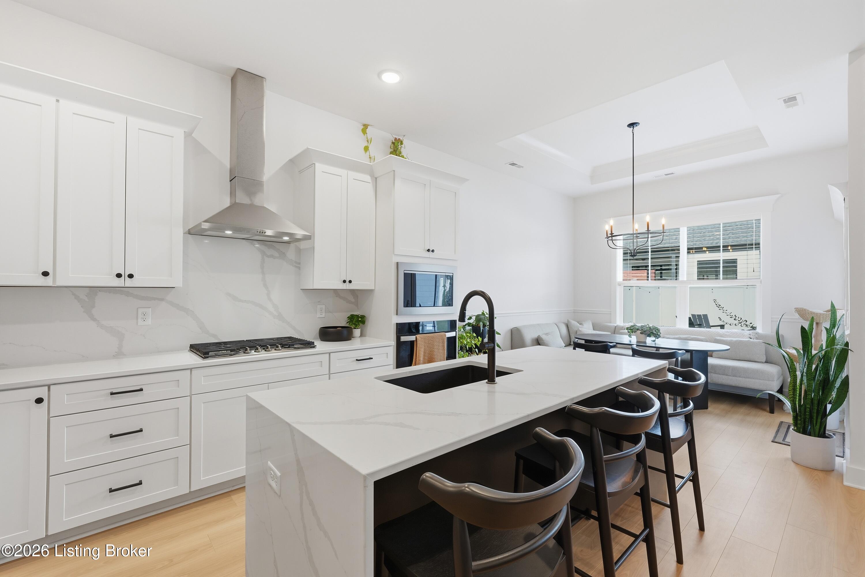 Bright white kitchen with a veined stone island, black bar stools, and an adjoining sitting area.