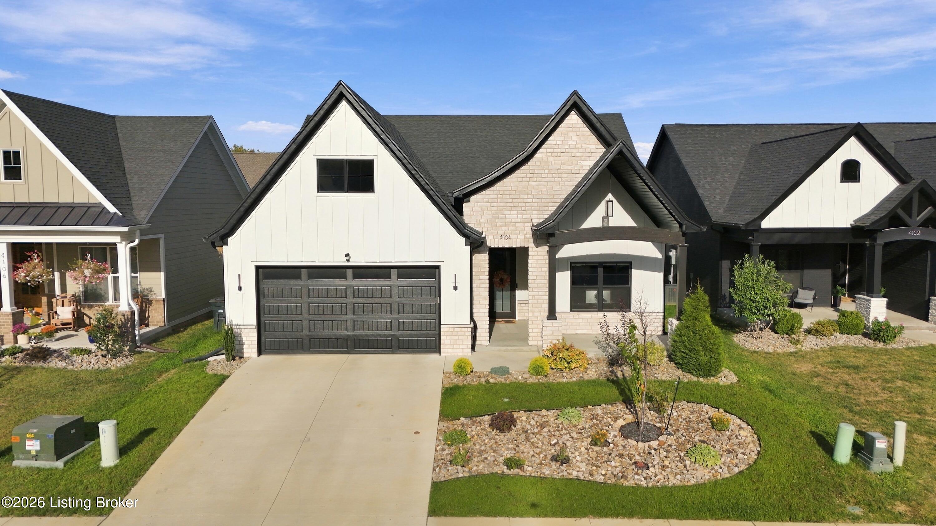 Front of a light brick-and-siding home with a dark garage door and landscaped yard.