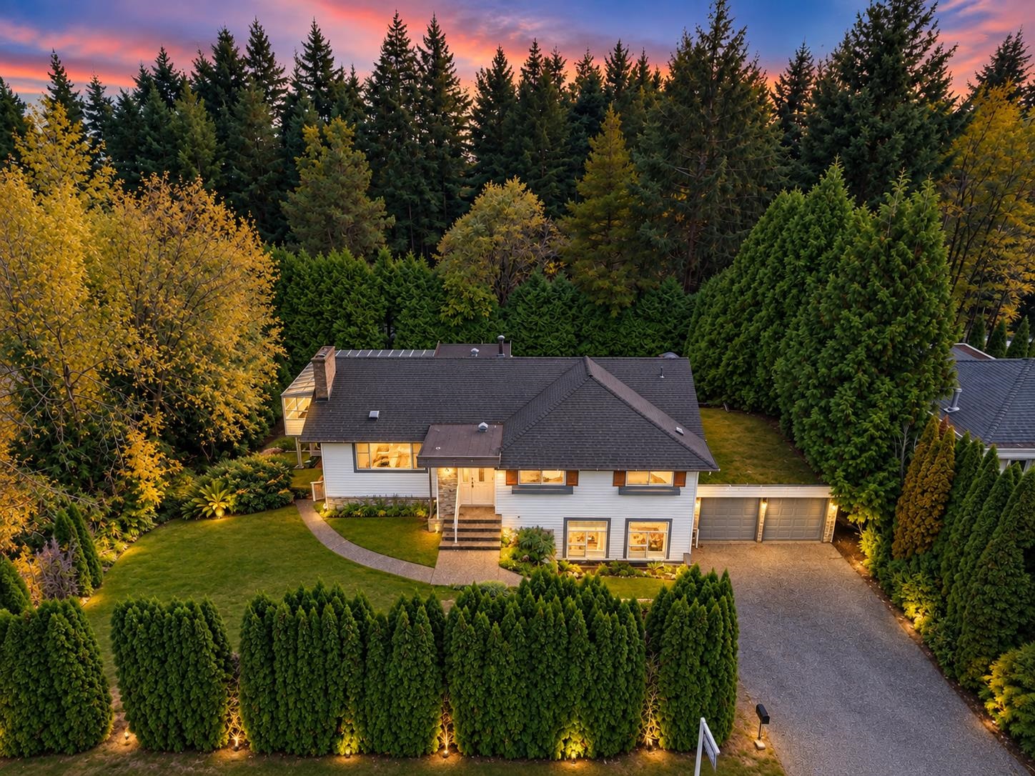 Aerial view of a two-story home with an attached double garage, surrounded by evergreens at sunset.